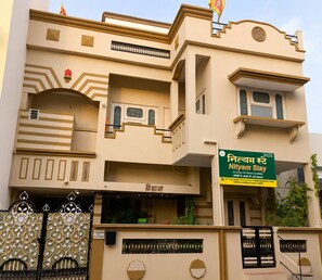 Un edificio de varios pisos con un letrero que indica 'Nityam Stay' y anuncia habitaciones disponibles.