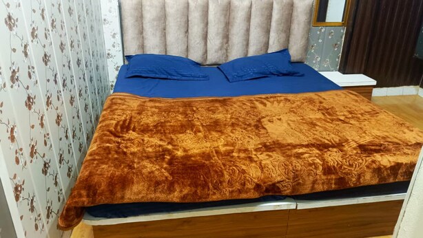 A bed with a headboard, a blue bedspread, and a brown blanket. - Hotel Nityam Stay (Ujjain)