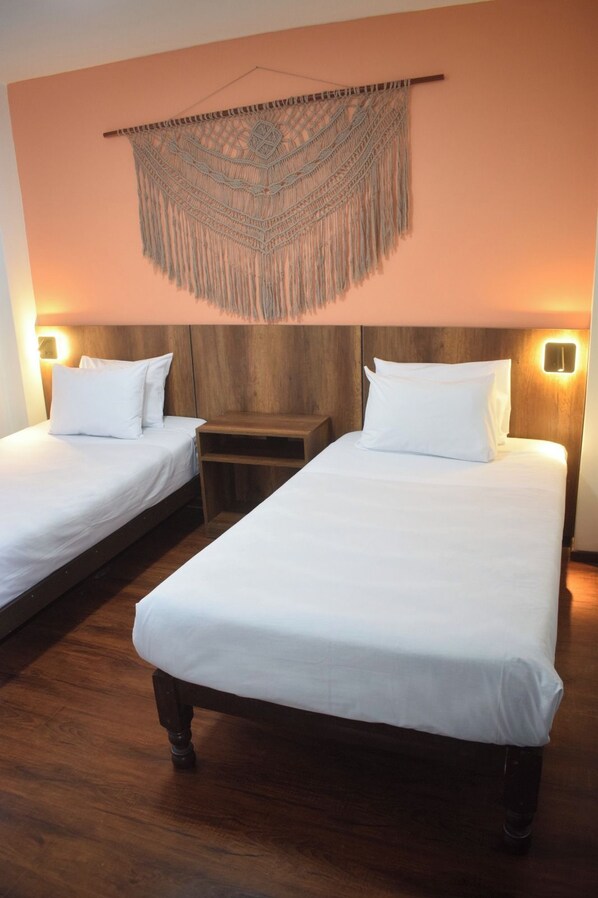 A hotel room with two single beds, wooden headboards, a wall hanging, and bedside lamps.