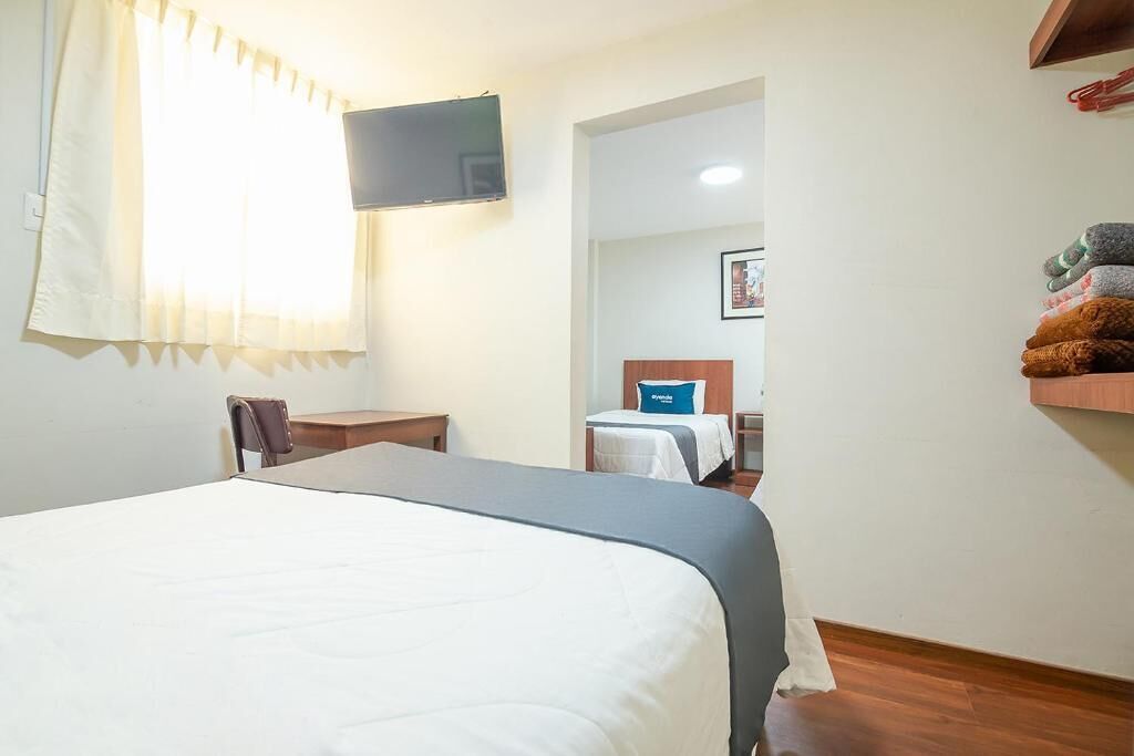 Una habitación de hotel con una cama, televisión montada en la pared, una mesita y una silla.