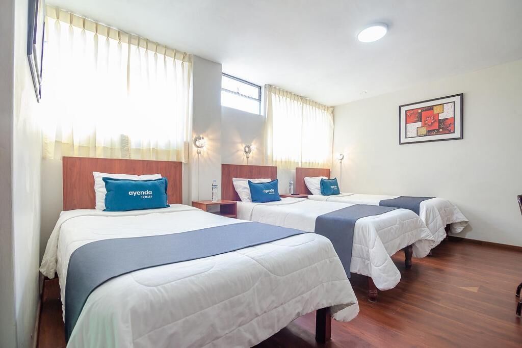 A hotel room with three beds, each with a blue headboard and a pillow labeled 'ayenda hotel'.