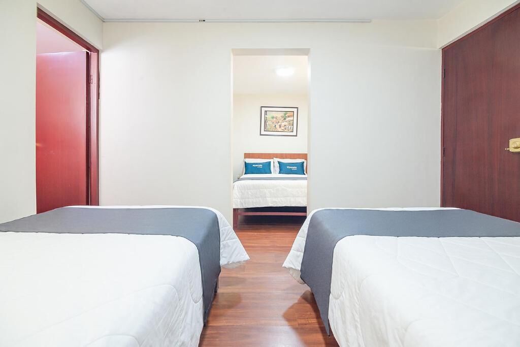 A hotel room with two single beds, a wooden floor, a red door, and a framed picture on the wall.