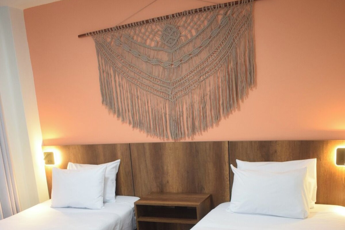 A hotel room with two beds, wooden headboards, and a macramé wall hanging.