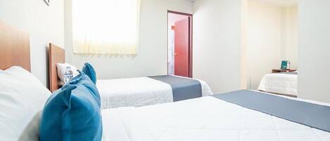 Habitación de hotel con dos camas, una ventana con cortinas, una puerta y una mesita con un libro.