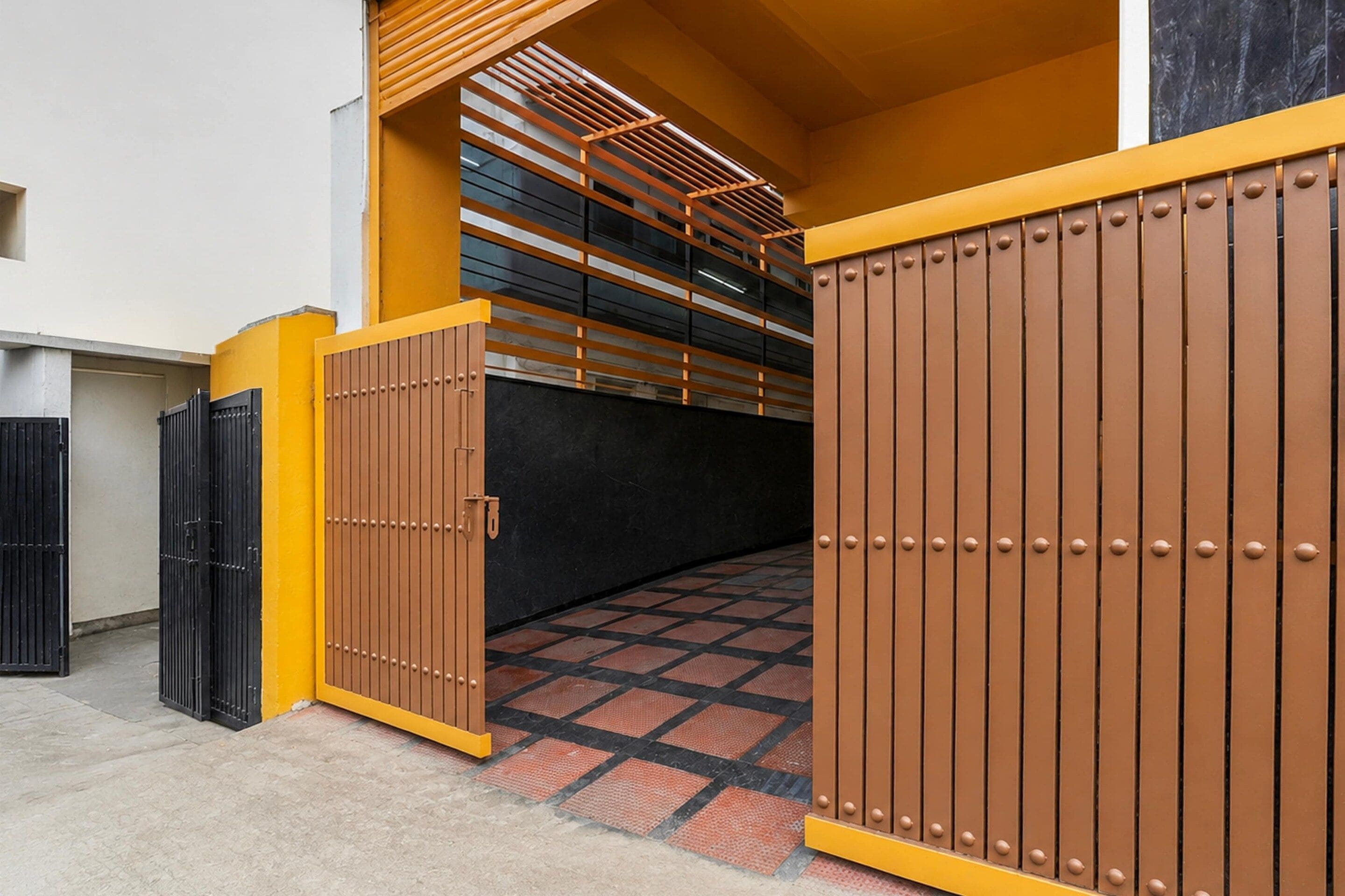 A gated entrance with a checkered floor pattern, a staircase with a wooden railing, and a wall with a black and yellow color scheme.