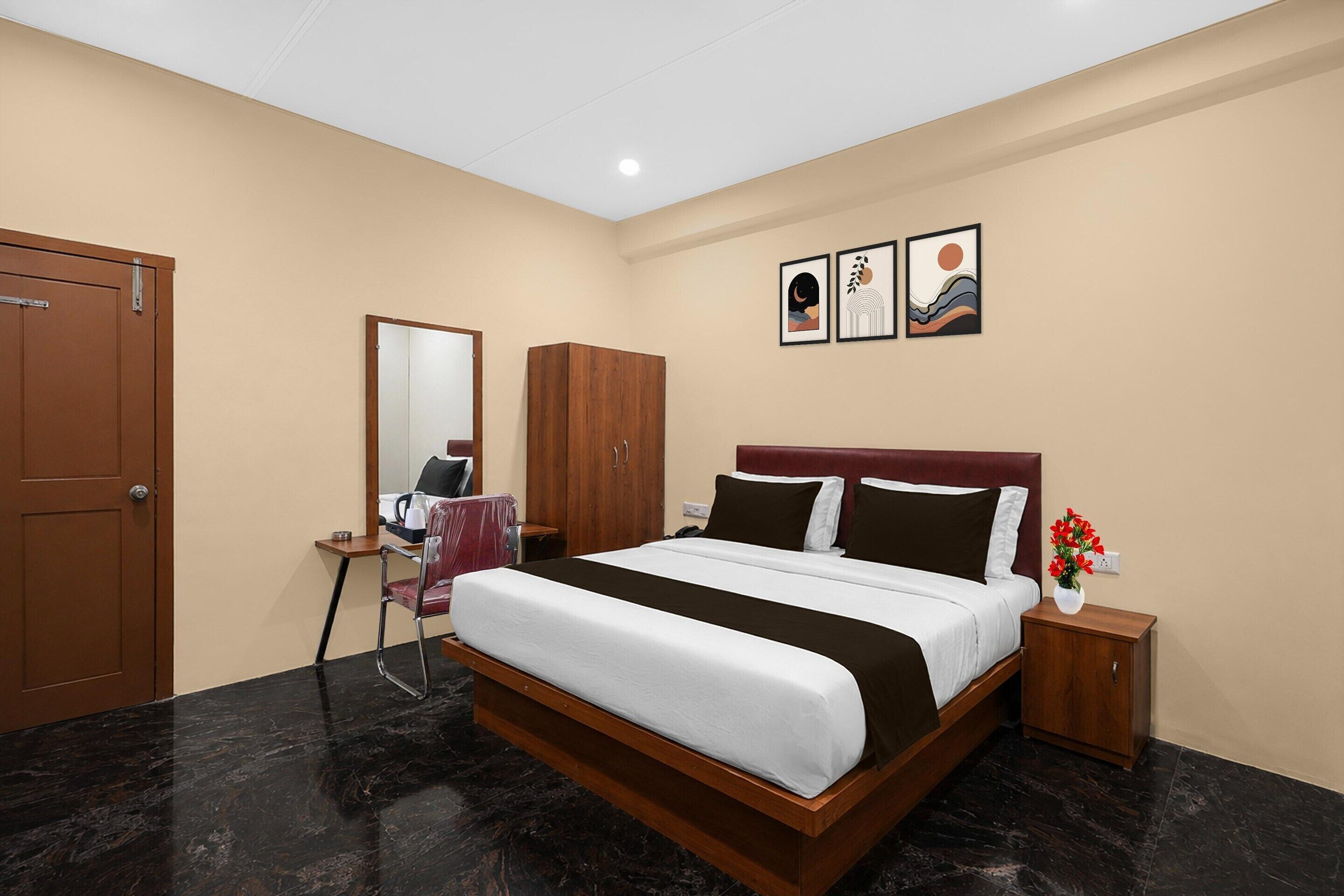 A hotel room with a bed, a desk, a chair, a wardrobe, and artwork on the wall.