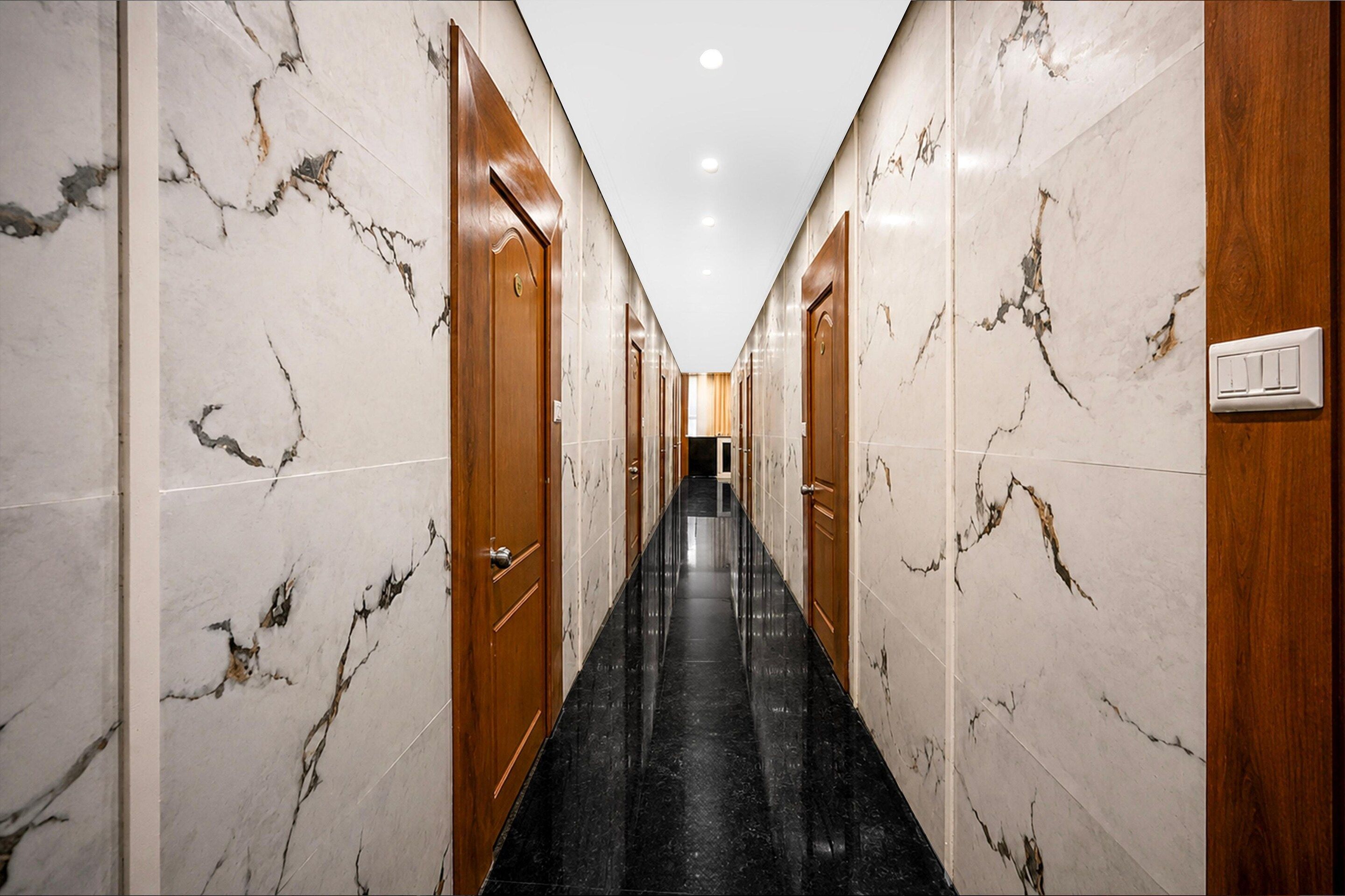 A hotel hallway with marble walls, wooden doors, and a black tiled floor.