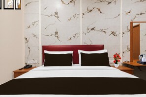A hotel room with a marble-patterned wall, a red headboard, a bed with white and black bedding, a nightstand with a phone, and a small table with a vase of flowers. - Deluxe Classic Residency (Bengaluru)