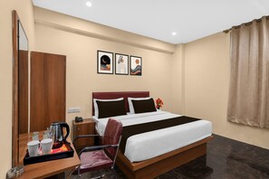 A hotel room with a bed, a desk with a kettle, cups, and a chair. There are three framed pictures on the wall. - Deluxe Classic Residency (Bengaluru)