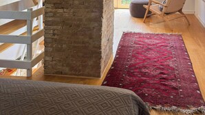 A loft bedroom with exposed brick, a white railing, a red patterned rug, and a view of greenery outside. - Historic house from 1827 on Langeland (Rudkøbing)
