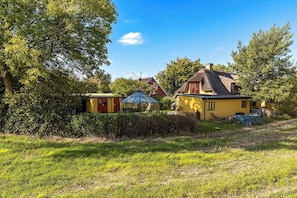Una casa rural con tejado de paja, rodeada de vegetación y un cielo despejado.