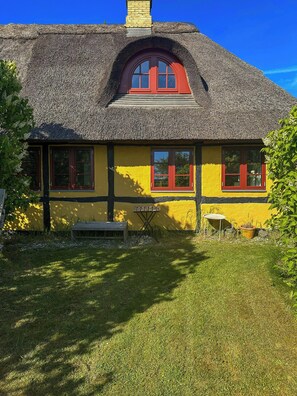 A thatched-roof house with yellow walls and red window frames.