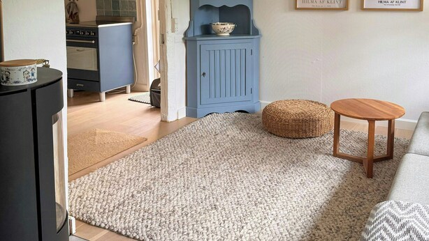 A living room with a sofa, a small round wooden table, a blue cabinet, and a kitchen in the background. - Historic house from 1827 on Langeland (Rudkøbing)