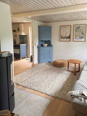 Una sala de estar con un sofá, una mesita redonda de madera, un armario azul y una cocina al fondo.