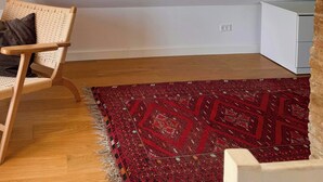 A room with a curved ceiling, a red patterned rug, a wicker chair, and a window with a view of a red building. - Historic house from 1827 on Langeland (Rudkøbing)
