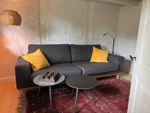 A modern living room with a grey sofa, two yellow cushions, a small round table with a decorative item, and a red patterned rug.