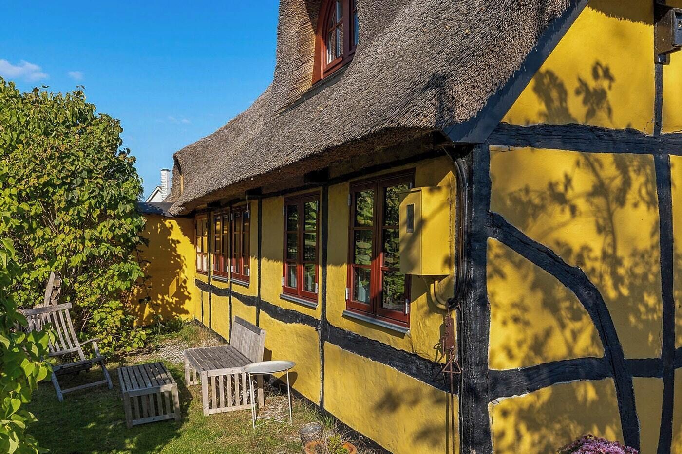 Une maison traditionnelle à colombages, avec un toit de chaume et une façade jaune.