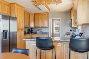 A kitchen with wooden cabinets, a stainless steel refrigerator, a coffee maker, and two black bar stools. - Sunlit Mountain Retreat Near Lakes & Ski Fun (Arnold)