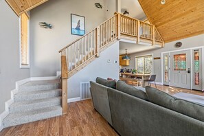 Un vaste espace de vie doté d’un escalier en bois, d’un canapé gris et d’un coin repas offrant une vue sur la cuisine.