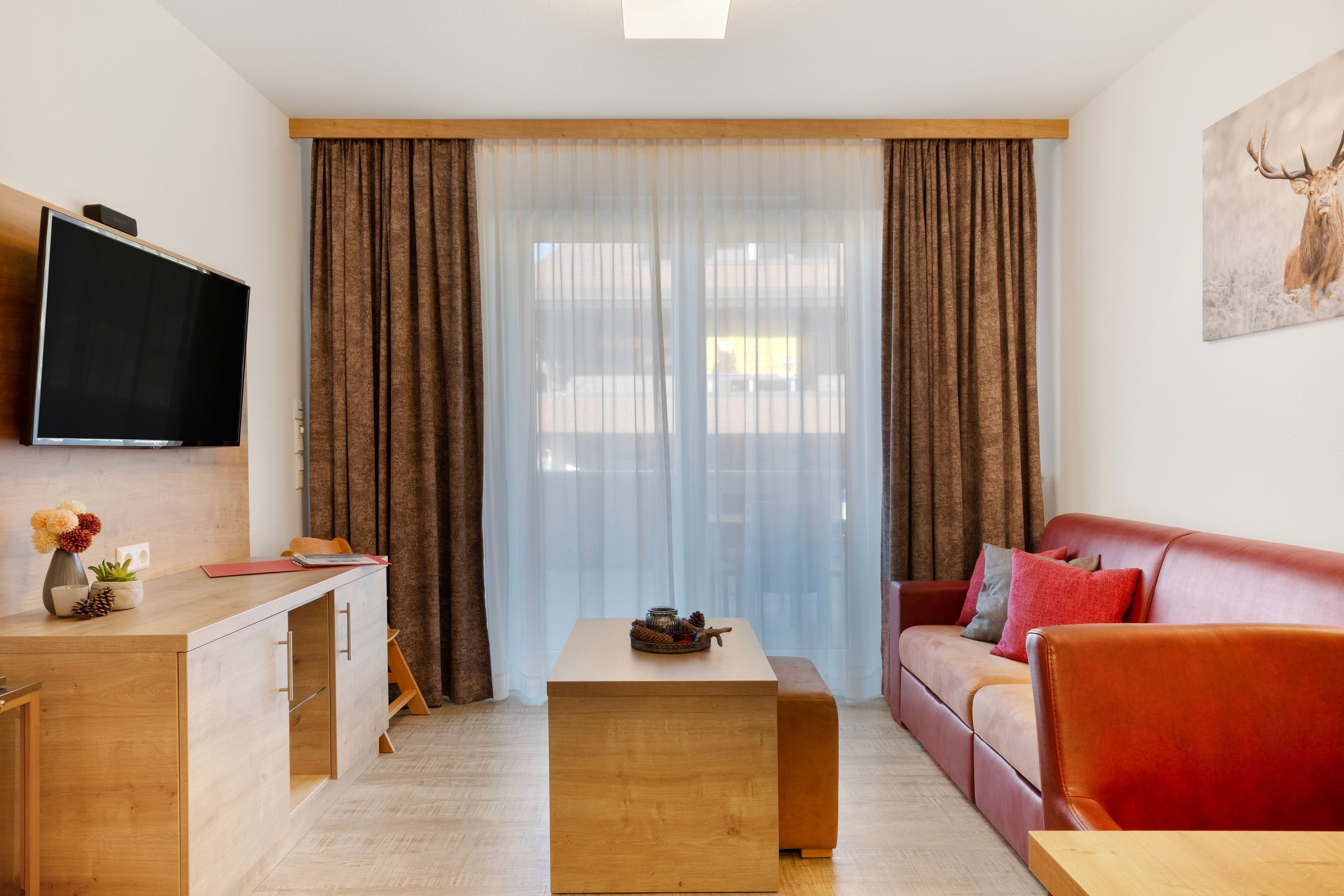 A modern living room with a sofa, a coffee table, a TV mounted on the wall, and a window with curtains.