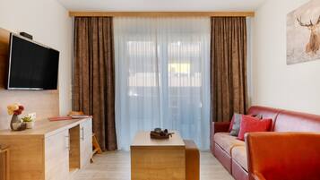 A modern living room with a sofa, a coffee table, a TV mounted on the wall, and a window with curtains.