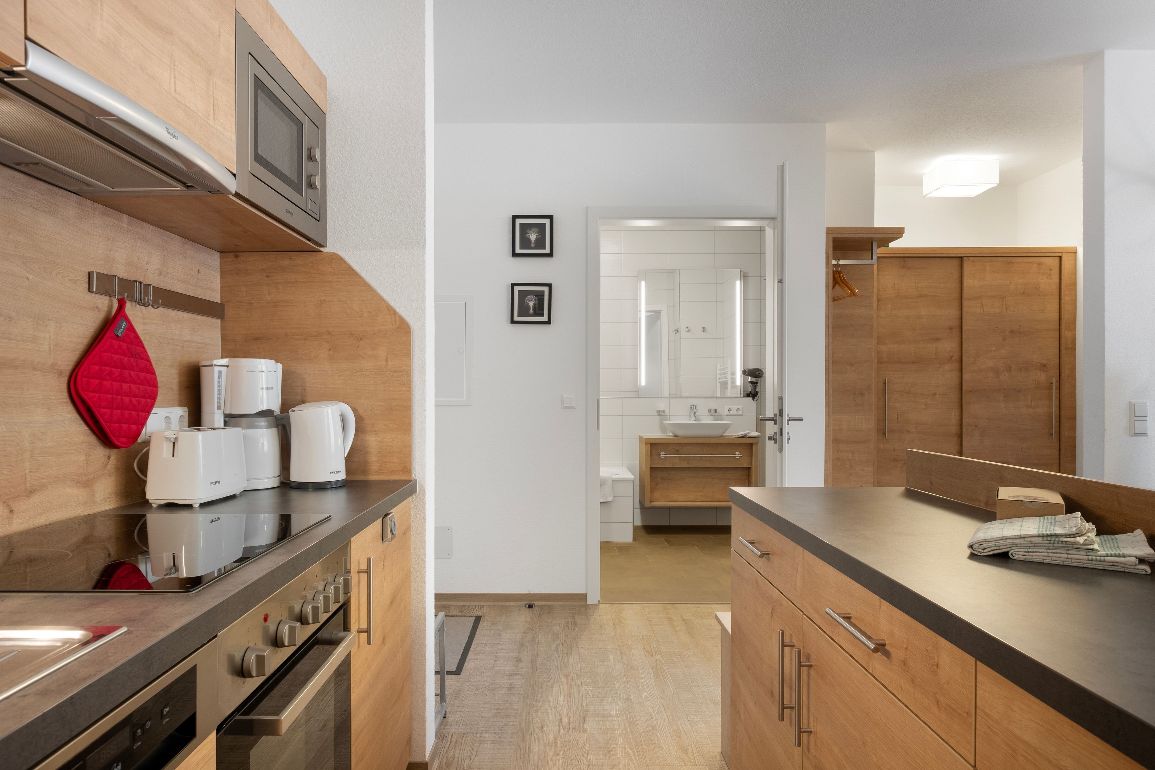 Een moderne keuken met roestvrijstalen apparatuur, houten kastjes en uitzicht op de aangrenzende badkamer.