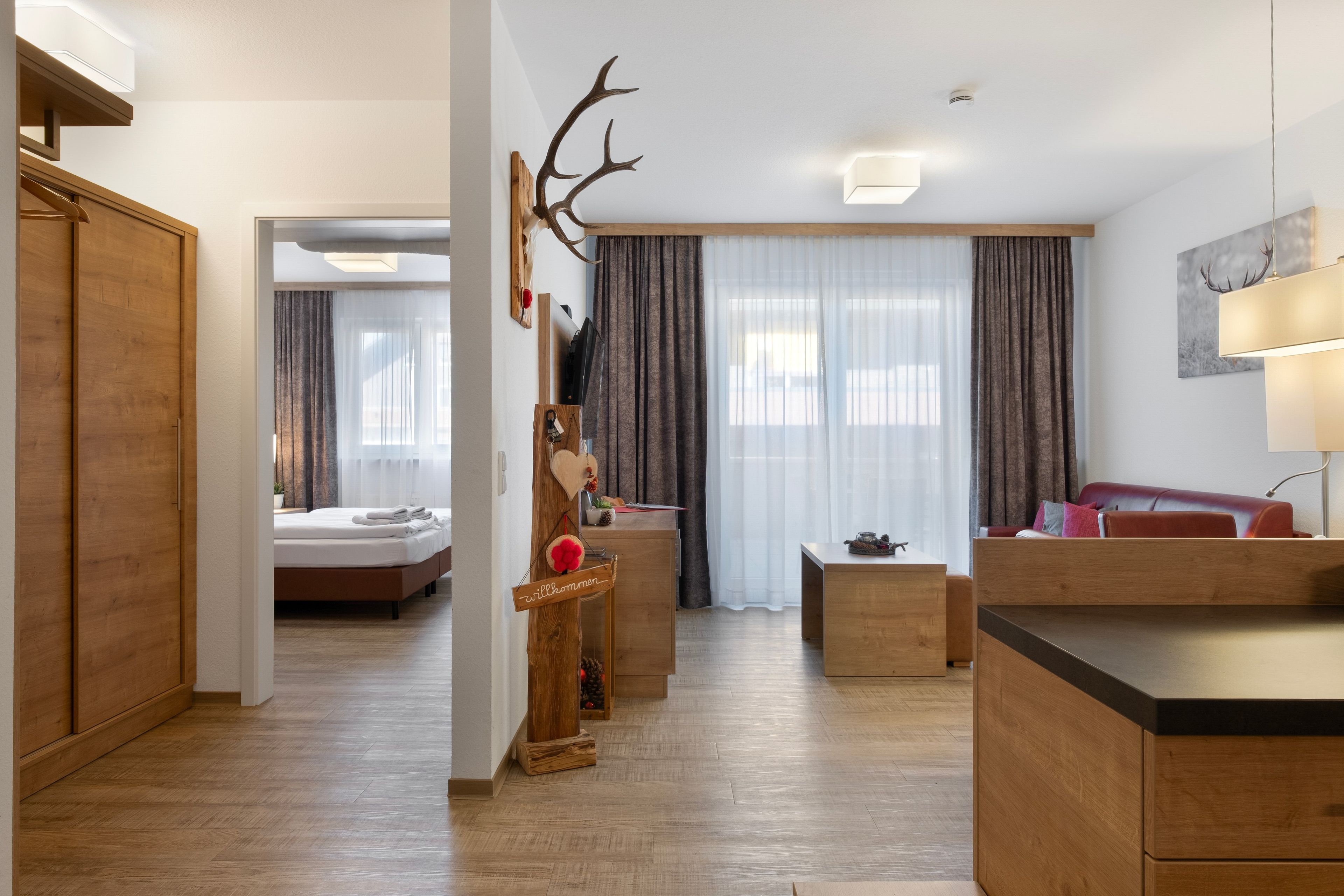 Een moderne hotelkamer met een houten vloer, een bed, een bureau, een bank en een groot raam met gordijnen.