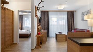 Een moderne hotelkamer met een houten vloer, een bed, een bureau, een bank en een groot raam met gordijnen.