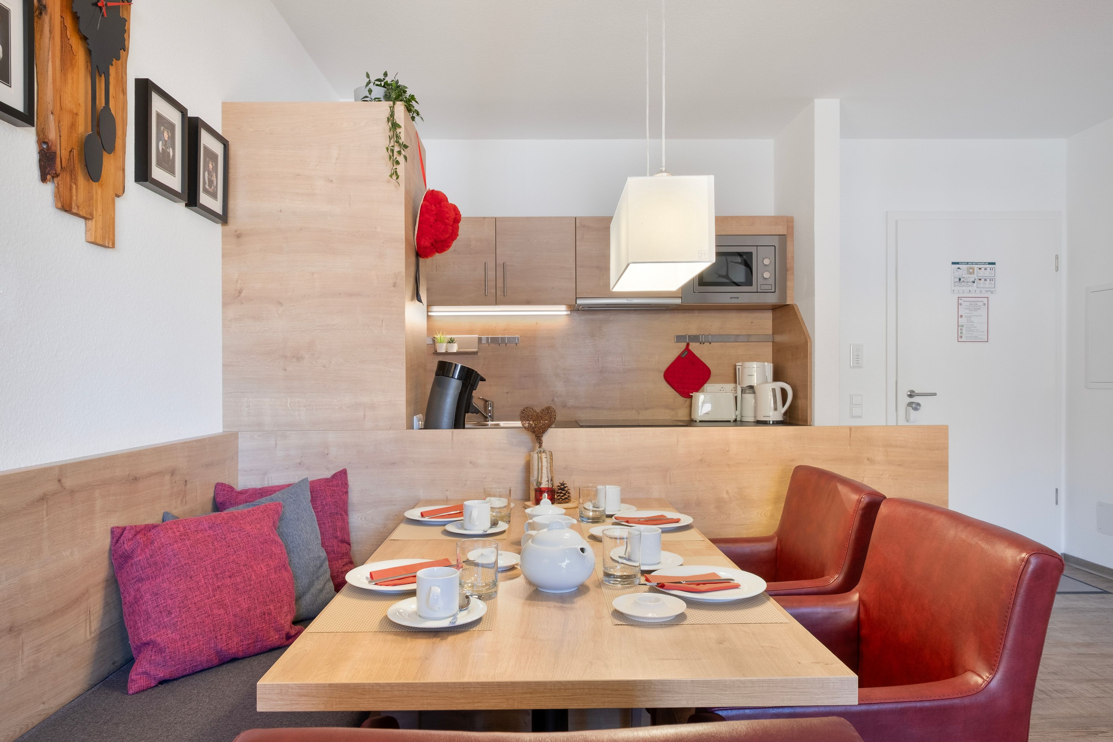 Een moderne eethoek met een houten tafel voor vier personen, een bank met kussens en een keuken op de achtergrond.
