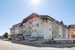 Un hotel de varios pisos con área de recepción, balcones y señalización para servicios como restaurante y centro de esquí.