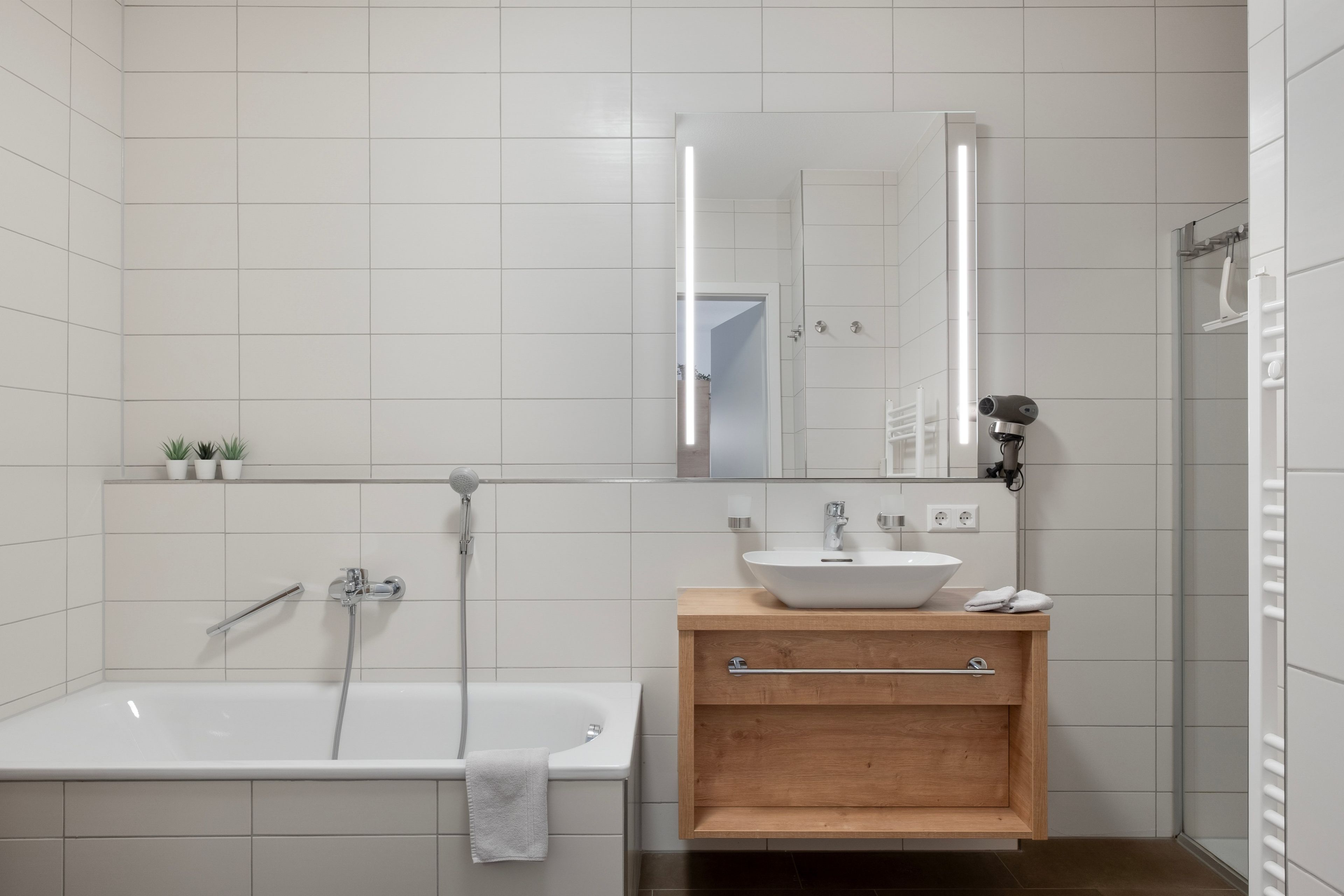 Un baño moderno con una bañera independiente, un tocador de madera con lavabo y un espejo sobre el tocador.