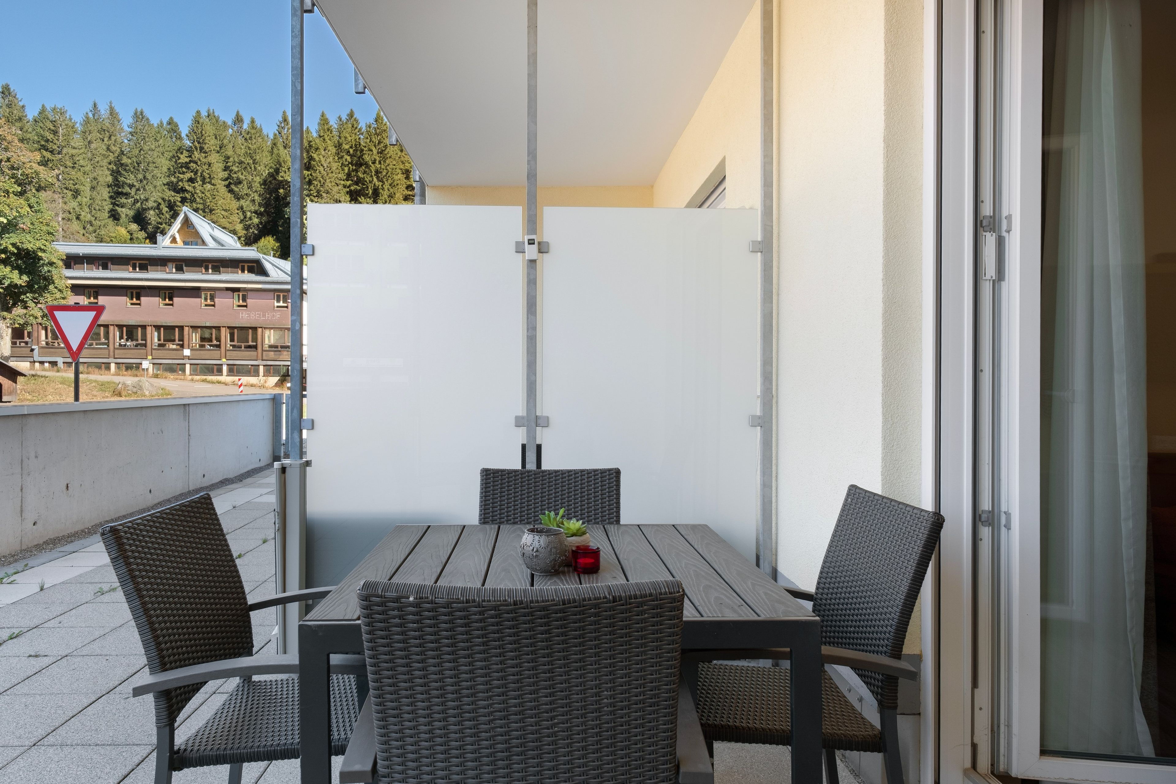 A balcony with a table and four chairs, a potted plant, and a red candle.