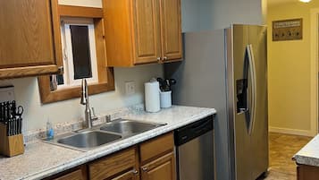 Une cuisine avec des meubles de rangement en bois, un évier en acier inoxydable, un lave-vaisselle et un réfrigérateur.
