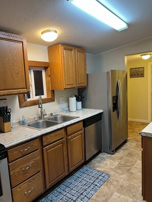 A kitchen with wooden cabinets, a stainless steel sink, a dishwasher, and a refrigerator.