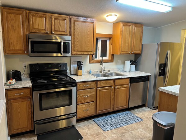A kitchen with wooden cabinets, stainless steel appliances, a microwave, a stove, a sink, and a refrigerator.