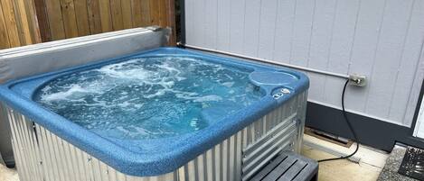 A hot tub with a blue edge, a wooden fence in the background, and a power outlet on the wall.