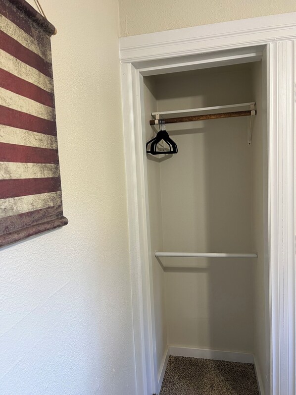 A small, enclosed closet with a wooden hanger rod and a white towel bar.