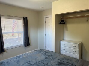 A bedroom with a bed, a dresser, a closet with a hanging rack, and a window with blinds.