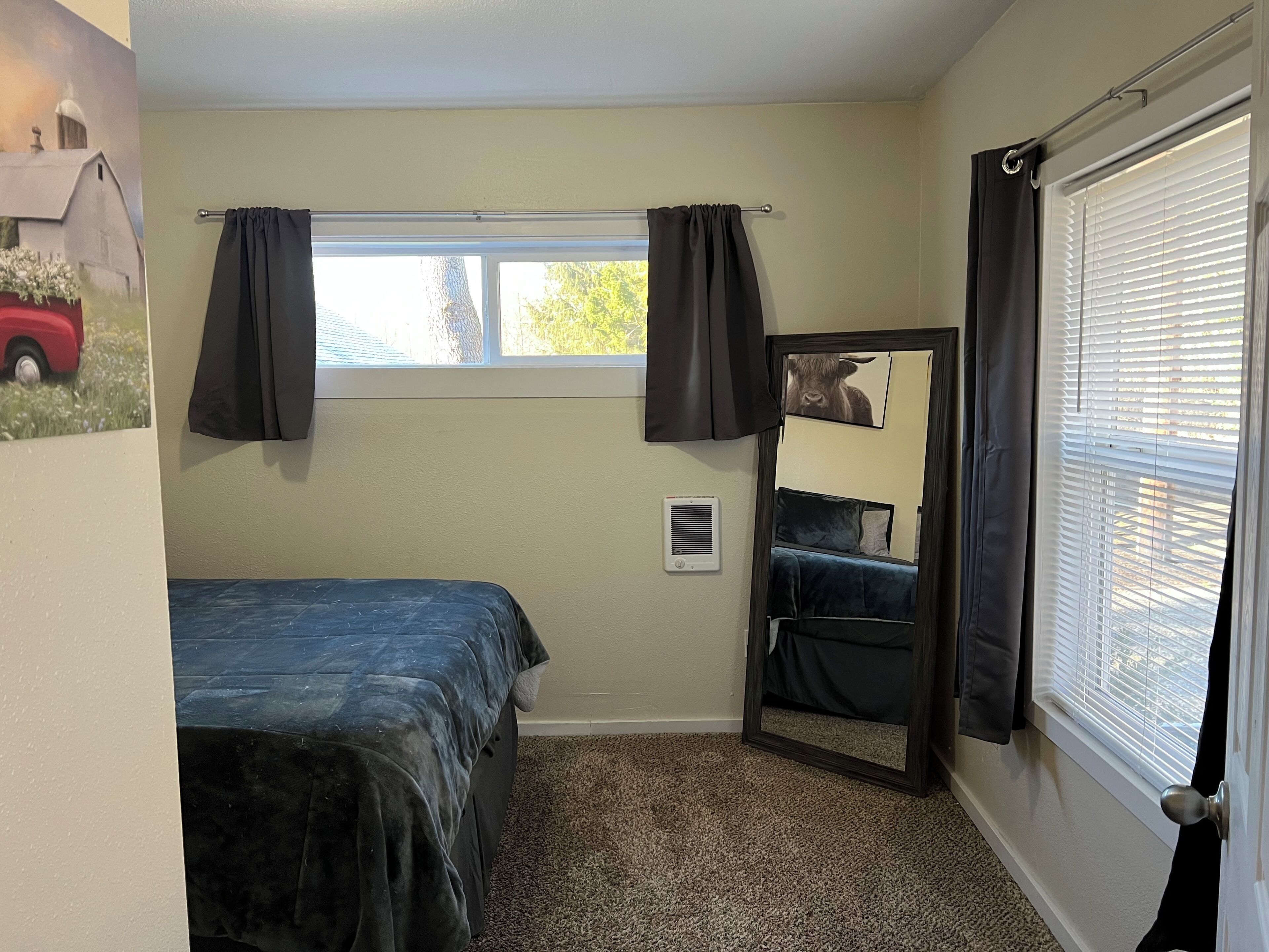 Une petite chambre avec un lit simple, une fenêtre, un miroir et une porte.