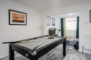 Ein Billardtisch mit Kugeln und Spielstangen, ein Fernseher und gerahmte Kunstwerke an den Wänden.