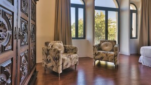 Una habitación con un aparador de madera, dos sillones estampados y amplios ventanales de arco.