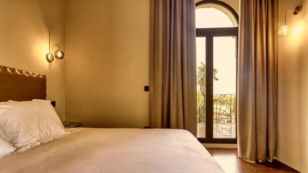 A hotel room with a large bed, a nightstand, a wall-mounted lamp, and a view of the outdoors through a door.