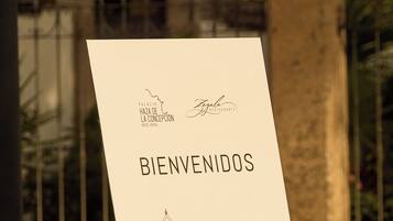 Un letrero de bienvenida con una ilustración de un edificio, colocado sobre un caballete al aire libre, con otro edificio en el fondo.