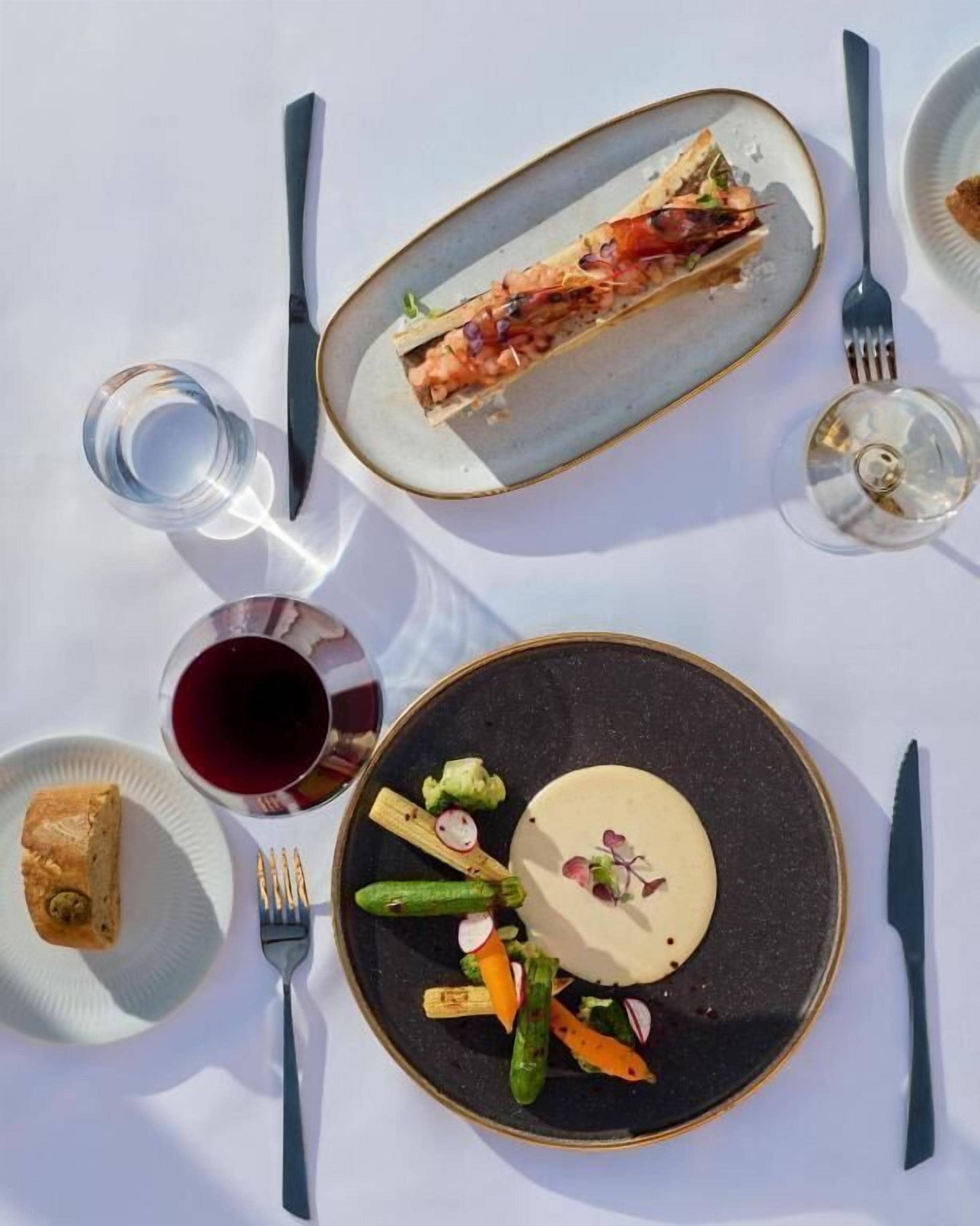 Una mesa de comedor con platos de comida, cubiertos y vasos.
