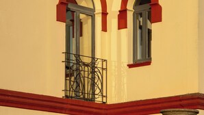 A building with two visible windows, each with a red frame and a balcony with metal railings.