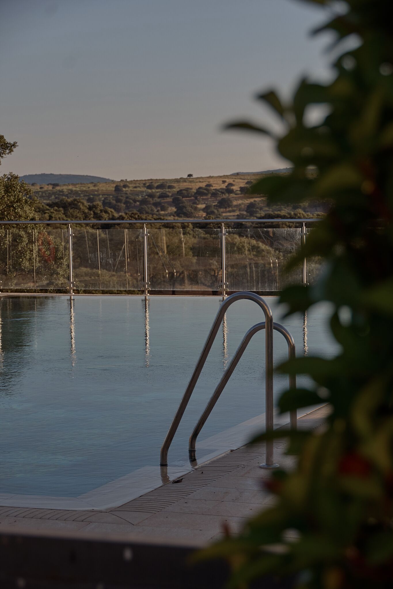 Una piscina con barandales metálicos y vistas a un puente y colinas al fondo.