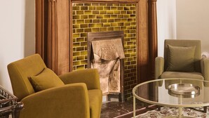 Una habitación con chimenea, dos sillones, una mesa de centro de vidrio y una alfombra estampada.
