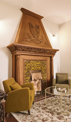 A room with a fireplace, two armchairs, a glass coffee table, and a patterned rug.