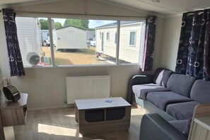 A caravan interior with a sofa, a table, and a view of mobile homes outside.