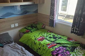 Un dormitorio pequeño con una cama individual superpuesta, una ventana con cortinas y una estantería en la pared.